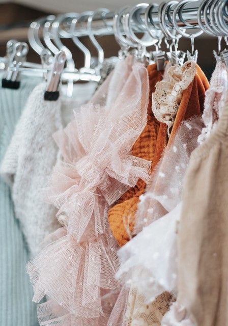 Détail de la garde-robe nouveau-né du studio de Cécile Muselet, avec des vêtements en tulle rose, dentelle, laine douce et tons naturels suspendus sur cintres