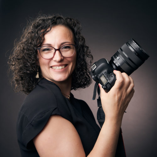 Portrait de Cécile Muselet, photographe professionnelle spécialisée en famille, grossesse et nouveau-né, souriante avec son appareil photo en studio