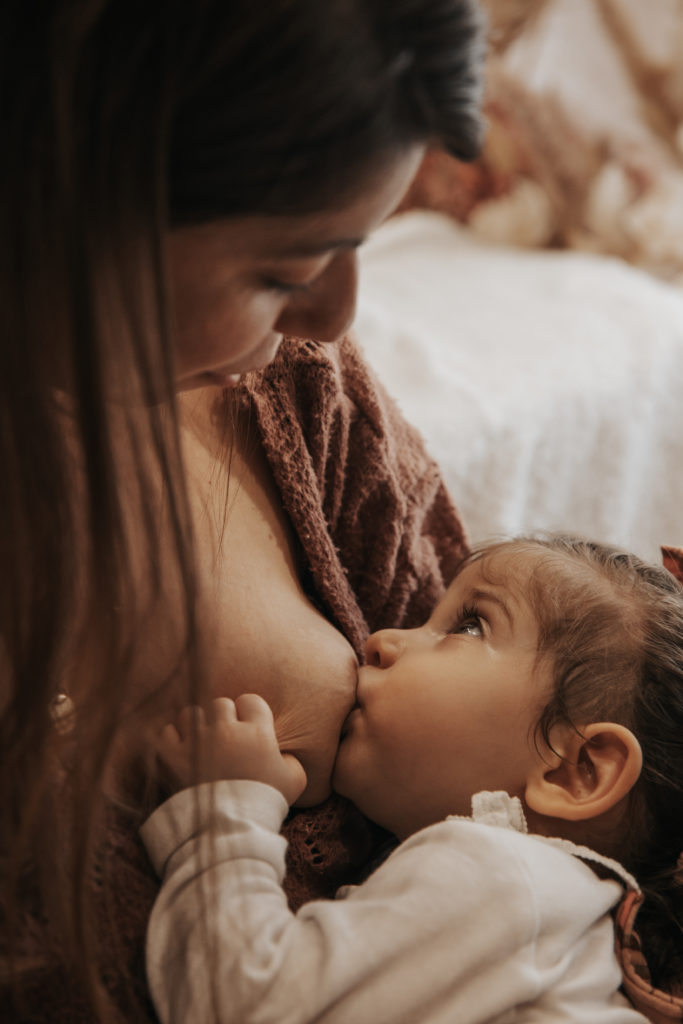 Maman allaitant tendrement sa petite fille, regard intense échangé entre elles, dans une ambiance douce et chaleureuse