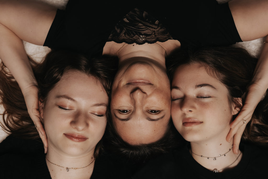 Portrait intime et doux d'une maman et ses deux filles allongées, visage contre visage