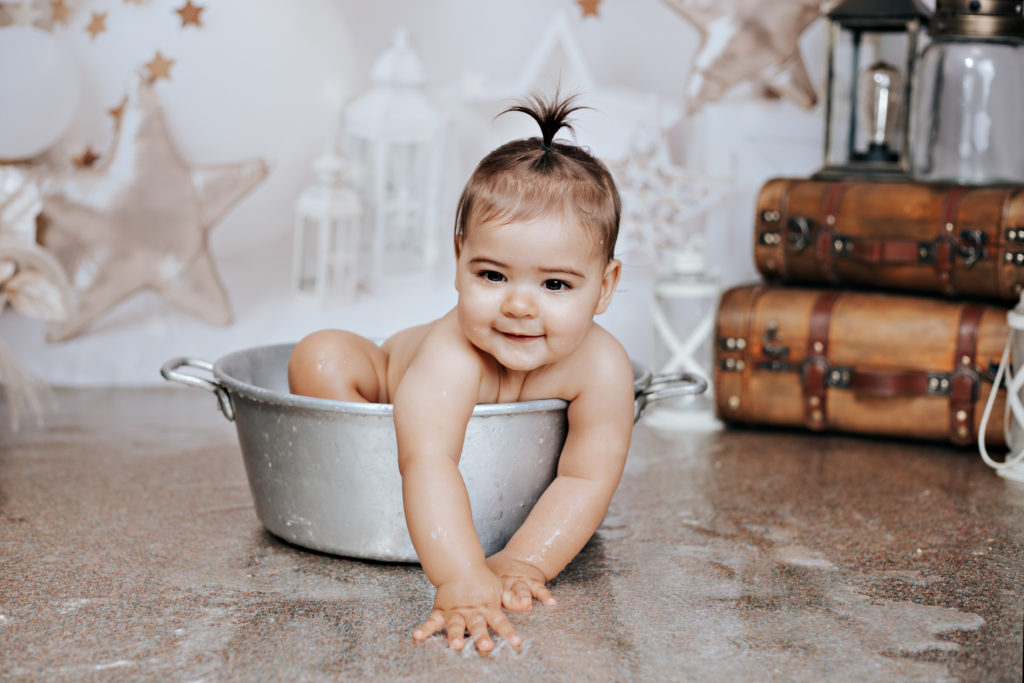 Bébé dans une bassine après son smash cake, moment de bain et de jeux Titre : bain de lait – séance anniversaire bébé