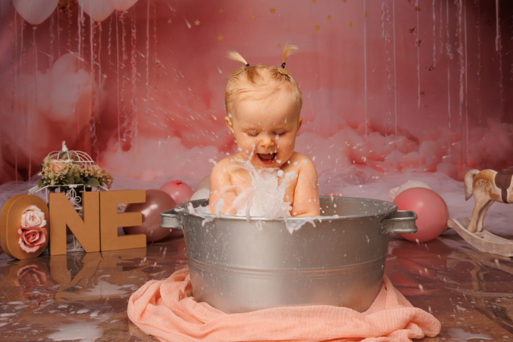 Bébé qui éclabousse dans un bain de lait lors de sa séance smash the cake