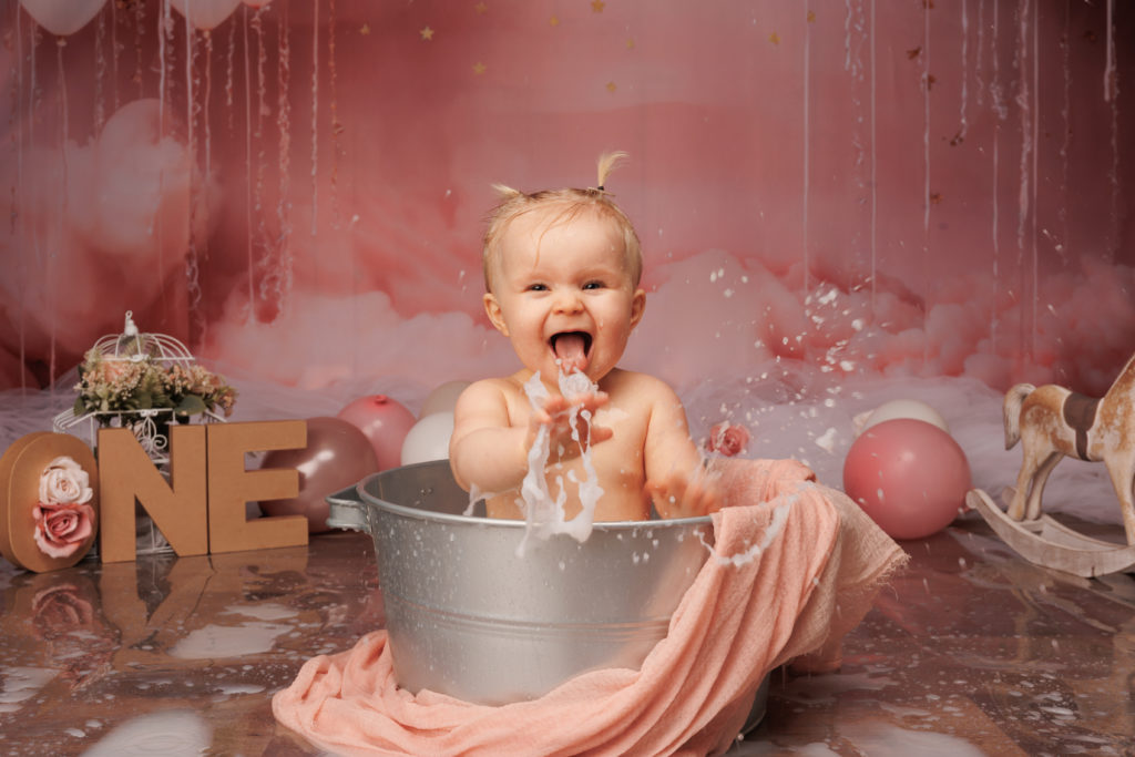 Bébé dans une bassine qui éclabousse en riant pendant un bain de lait