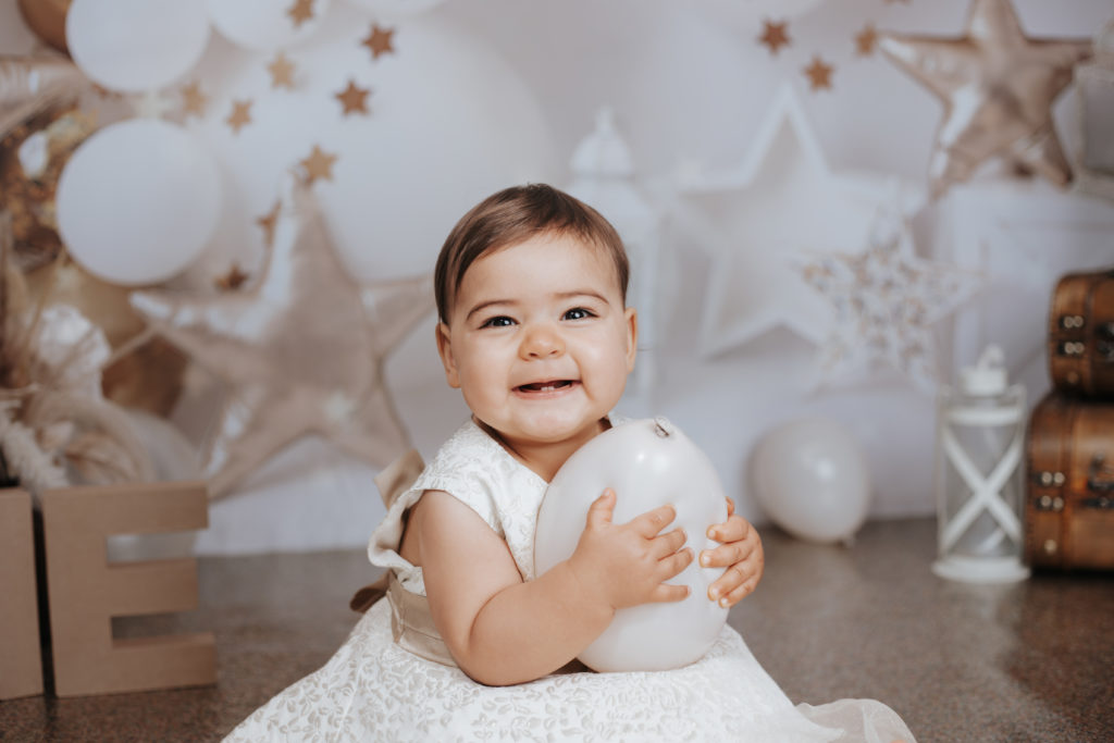 Bébé souriant tenant un ballon blanc lors de sa séance photo d’anniversaire dans un décor étoilé