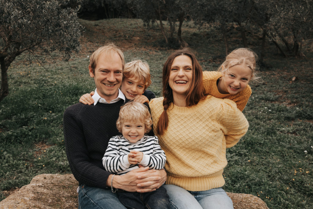 Famille souriante posant assise sur un rocher dans un cadre naturel verdoyant