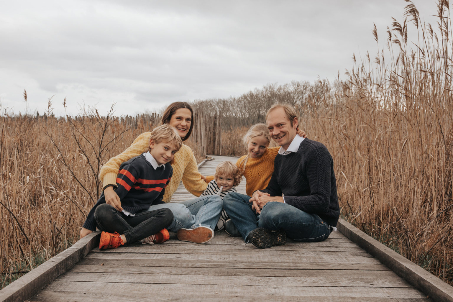 Famille de cinq posant sur un ponton en bois entouré de roseaux, ambiance automnale