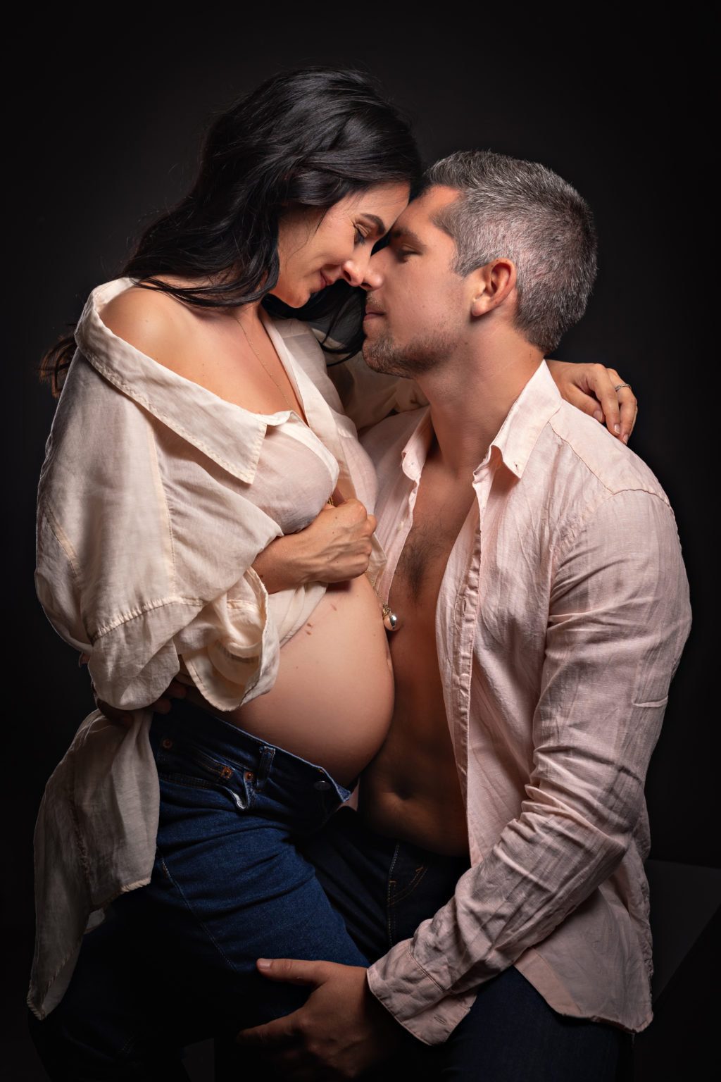 Couple tendre et complice en séance photo grossesse en studio, front contre front, échangeant un moment de douceur.