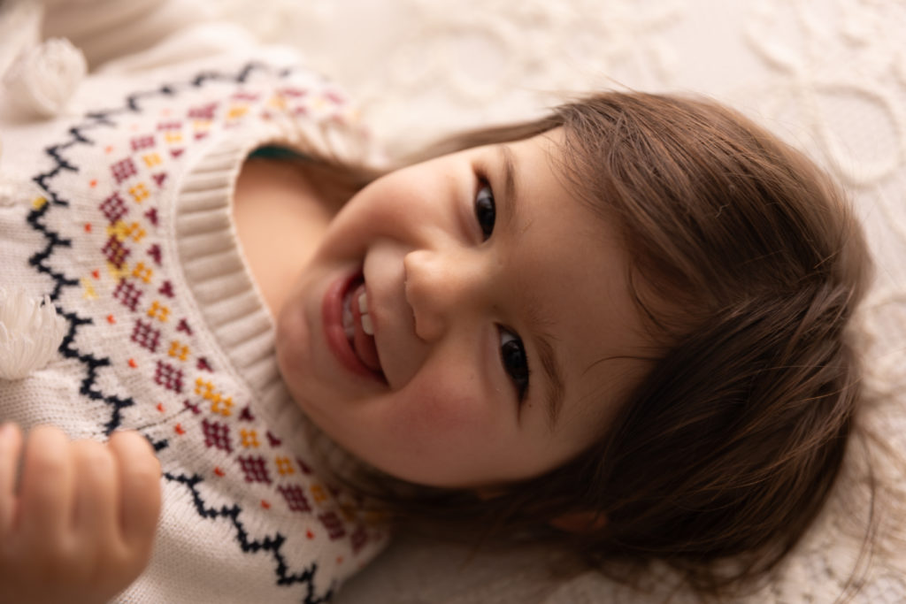 Petite fille qui rit allongée sur un lit, capturée dans un moment de joie spontanée