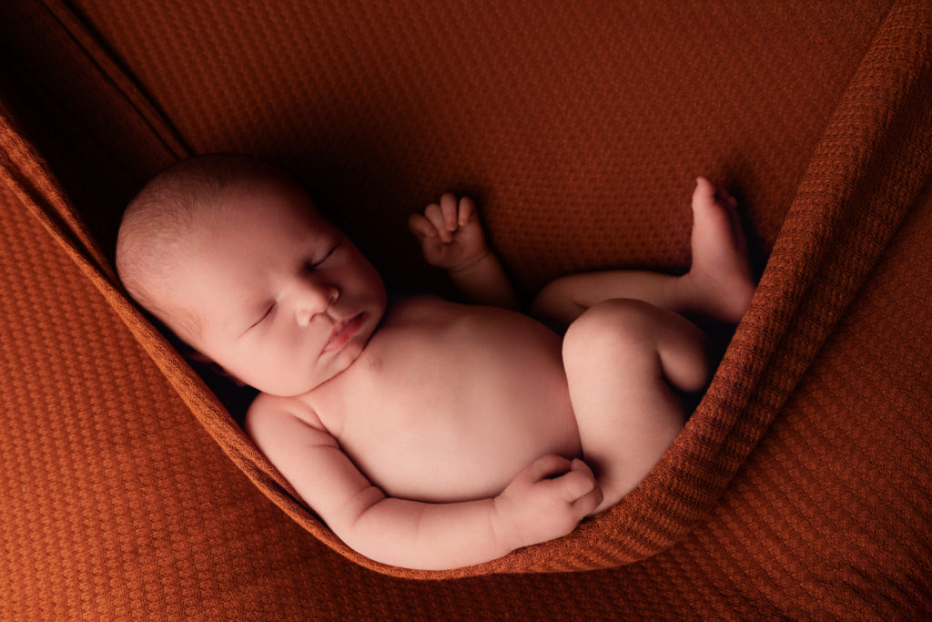 Nouveau-né allongé dans un tissu terracotta, photo naissance studio cocooning Provence
