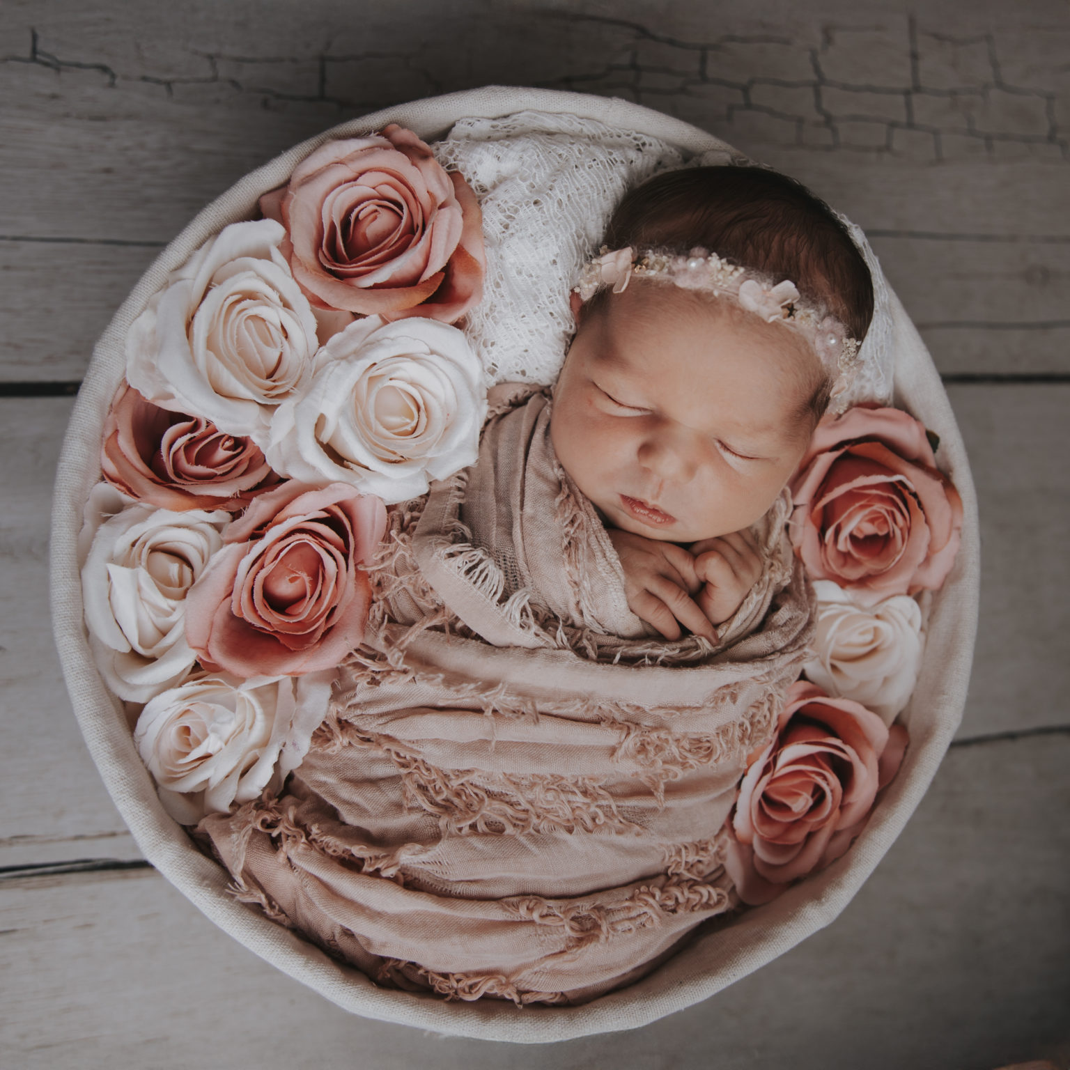 Nouveau-né emmailloté entouré de fleurs roses et blanches dans un panier