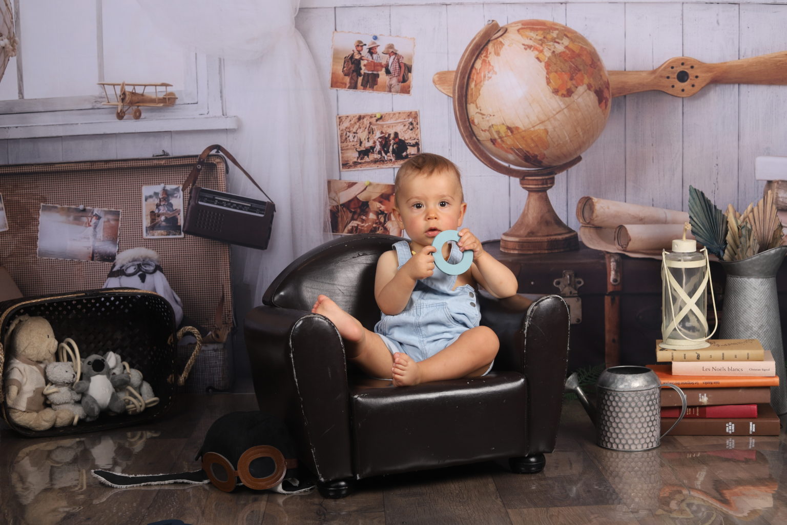 Bébé assis dans un fauteuil en cuir tenant un chiffre 0 bleu dans un décor de voyage vintage