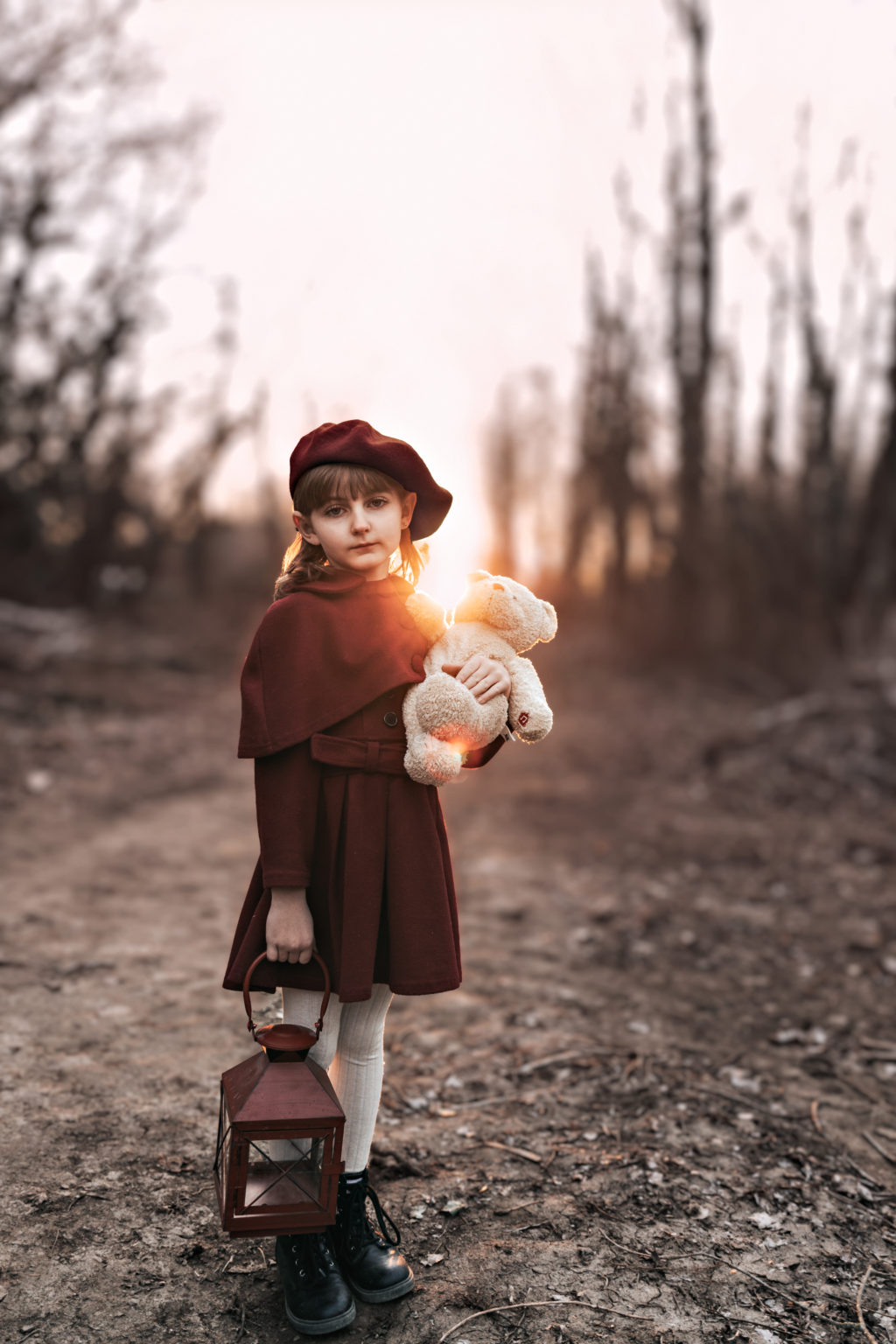 Petite fille au regard rêveur, tenant un nounours et une lanterne au coucher du soleil