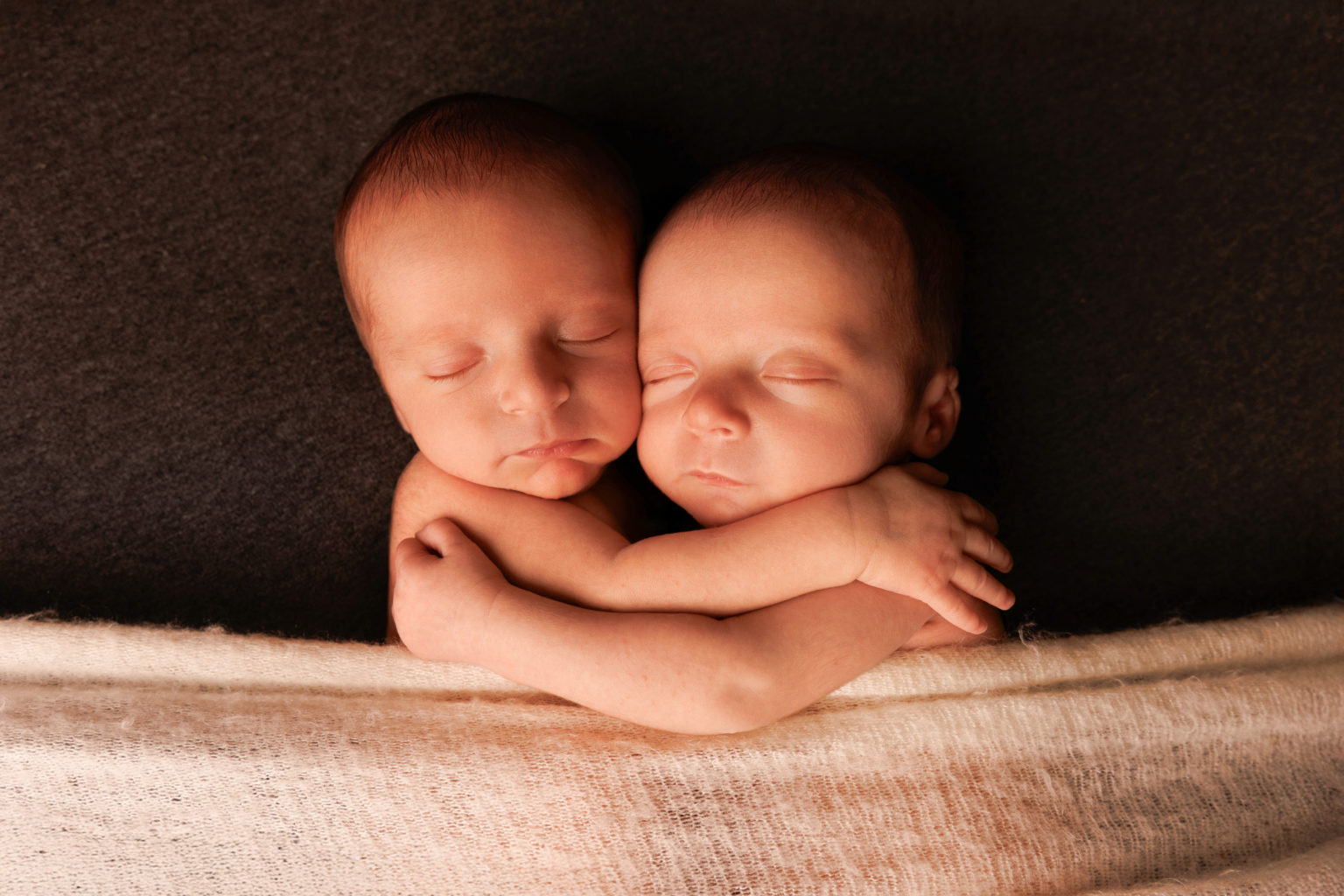 Deux bébés jumeaux endormis, enlacés tendrement l’un contre l’autre.