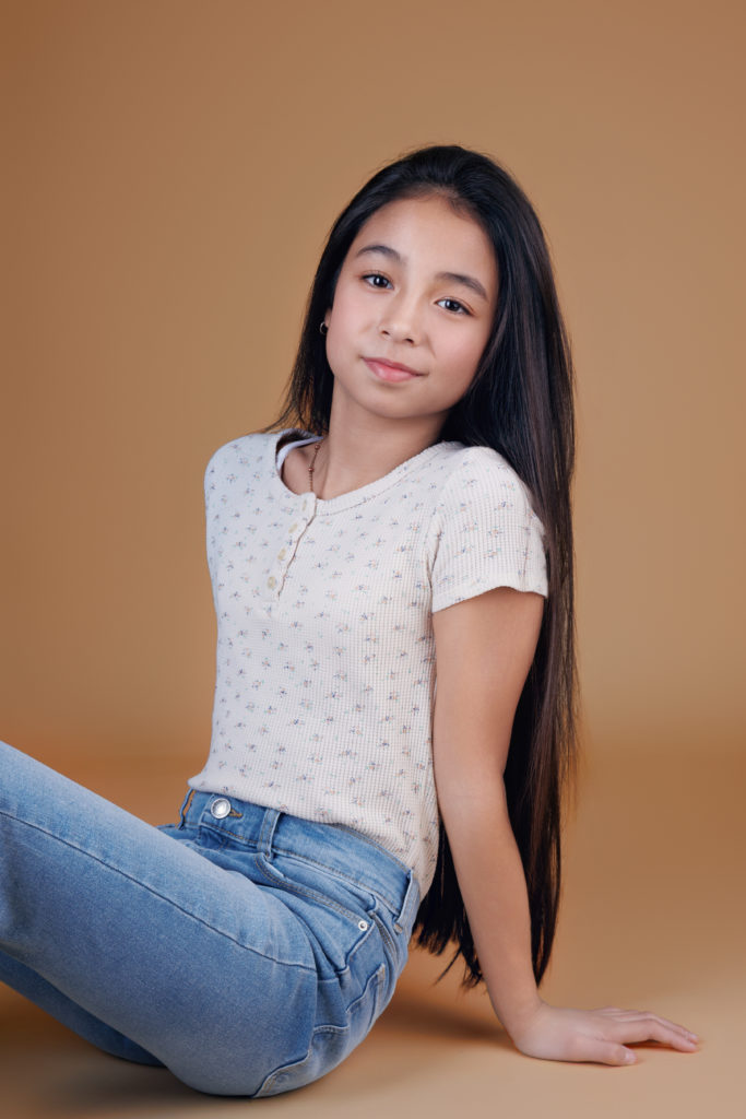 Portrait d’une adolescente souriante assise sur fond beige