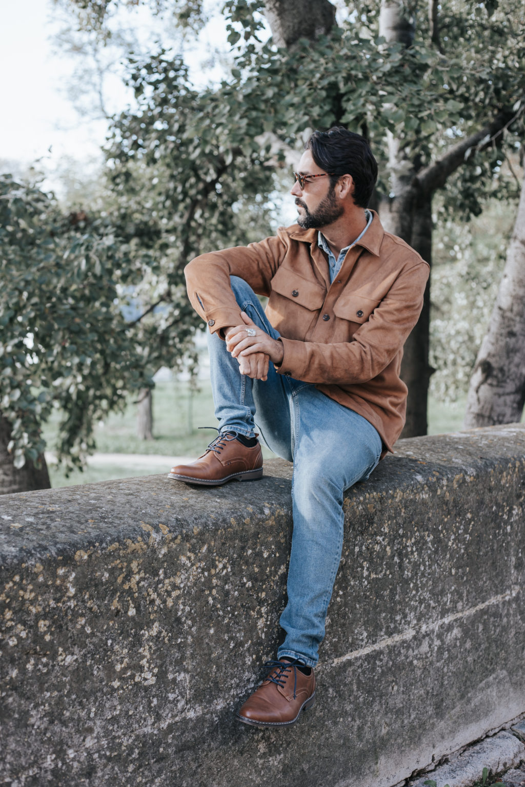 Homme assis sur un muret en pierre, regard tourné vers l’horizon, en tenue casual chic