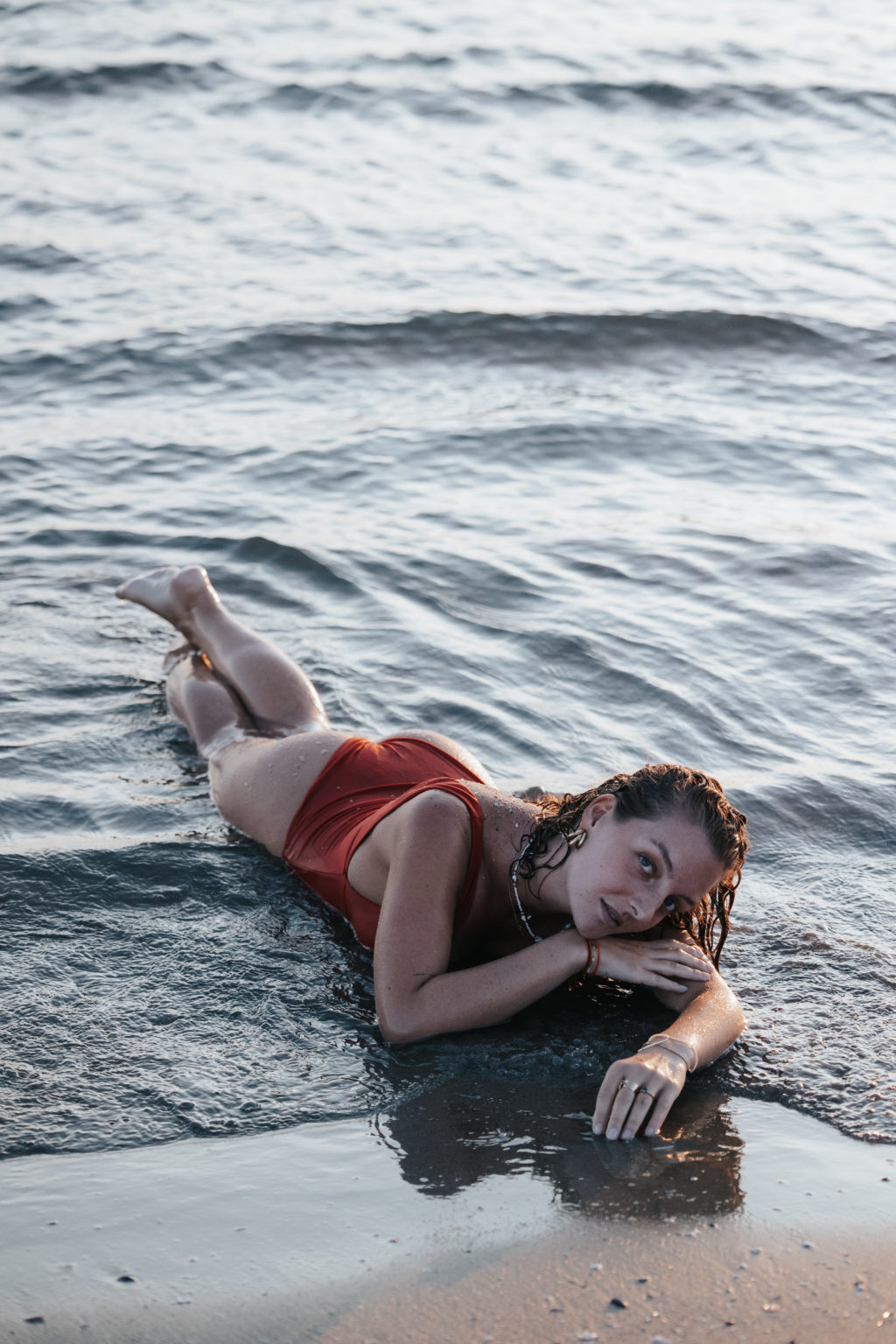 Femme allongée sur le sable, en maillot, dans l’eau au bord de la mer