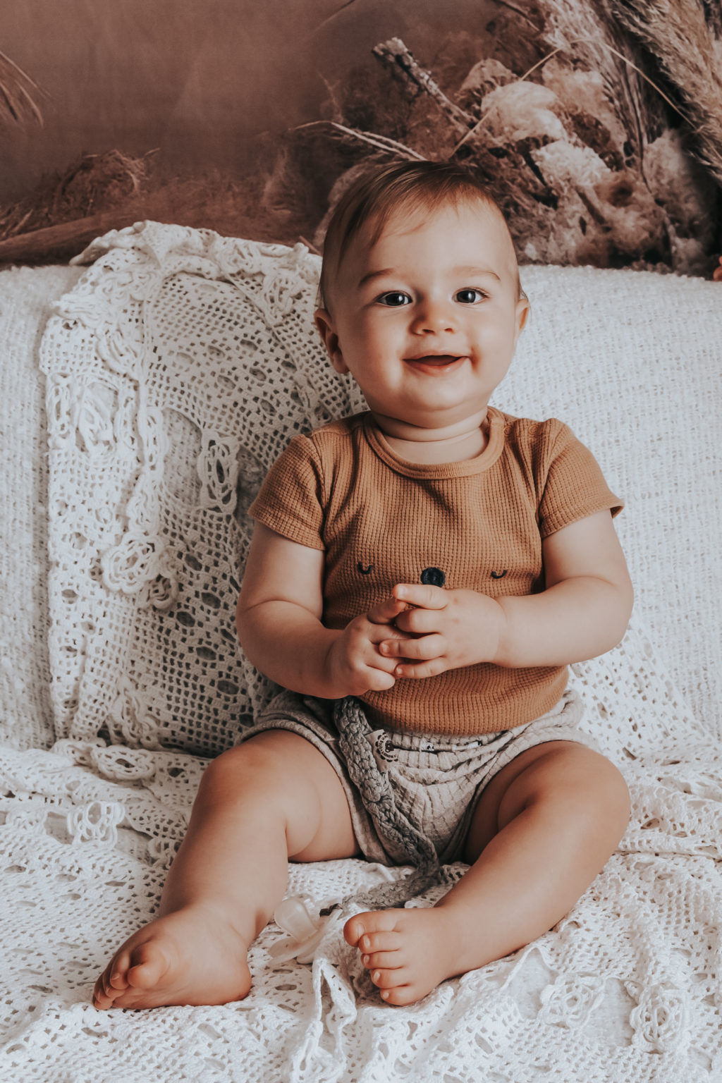 Bébé souriant assis sur un plaid en dentelle, ambiance naturelle et vintage