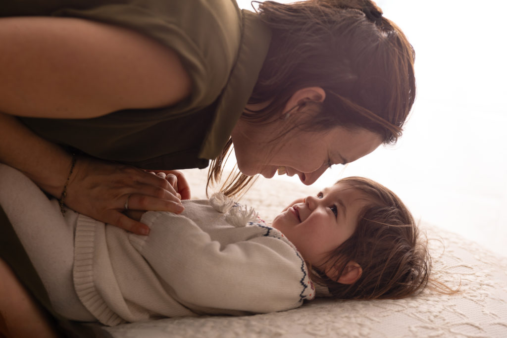 Petite fille en manteau bordeaux tenant son ours en peluche dans un décor d’automne