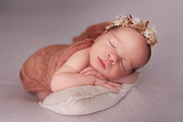 Séance photo nouveau-né en studio à Rognonas, bébé endormi posé sur un coussin avec bandeau fleuri, lumière douce et tons naturels