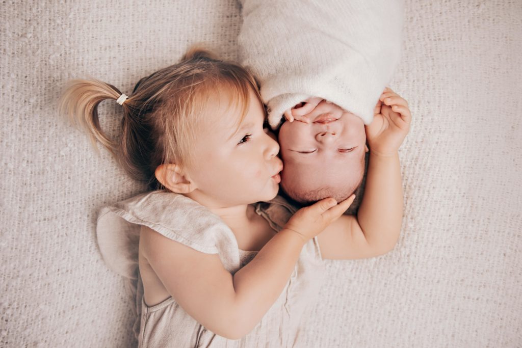 Grande sœur embrassant un nouveau-né allongé, photo famille naissance studio Provence